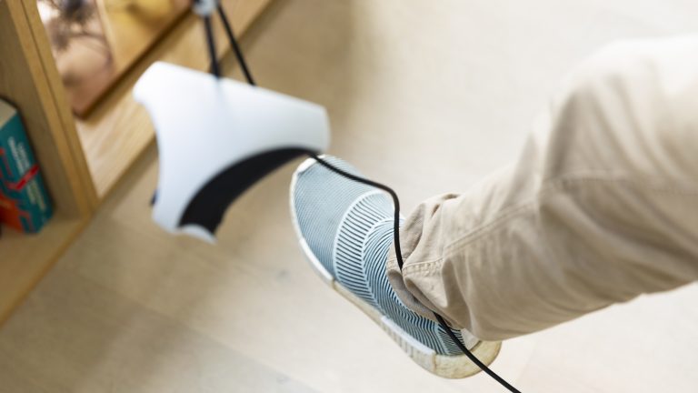 Um einen Fuß ist das Kabel der PSVR 2 gewickelt. Im Vordergrund hängt unscharf ein Sense-Controller ins Bild. Um einen Fuß ist das Kabel der PSVR 2 gewickelt. Im Vordergrund hängt unscharf ein Sense-Controller ins Bild.