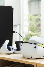 Eine PSVR 2 liegt neben einer PlayStation 5 auf einem Holzregal.