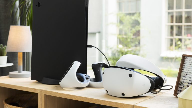 Eine PSVR 2 liegt neben einer PlayStation 5 auf einem Holzregal.