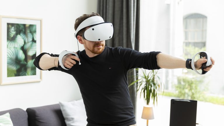 Eine Person steht in einem Wohnzimmer und trägt eine PlayStation VR 2. Eine Person steht in einem Wohnzimmer und trägt eine PlayStation VR 2.