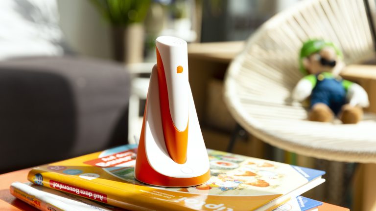 Ein Tiptoi-Stift steht in der dazugehörigen Ladestation auf einem Stapel Tiptoi-Bücher.