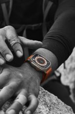 Eine Person beim Klettern trägt eine Apple Watch Ultra, die das exklusive Wegweiser-Zifferblatt trägt. Das Foto ist bis auf die Uhr in Schwarzweiß gehalten.