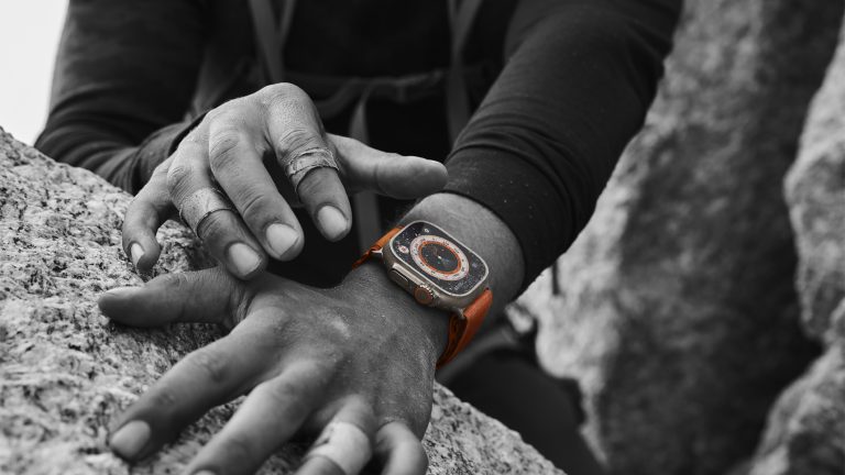 Eine Person beim Klettern trägt eine Apple Watch Ultra, die das exklusive Wegweiser-Zifferblatt trägt. Das Foto ist bis auf die Uhr in Schwarzweiß gehalten.