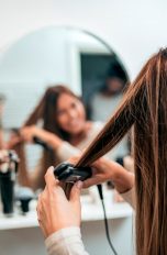 Eine Person steht vor einem Spiegel und glättet sich eine Haarsträhne.