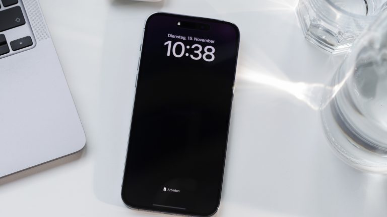 Ein iPhone 14 Pro Max liegt neben einem MacBook auf einem Schreibtisch.