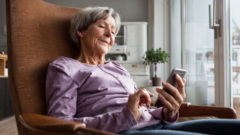 Eine Person sitzt auf einem Sessel und schaut auf ein Smartphone.