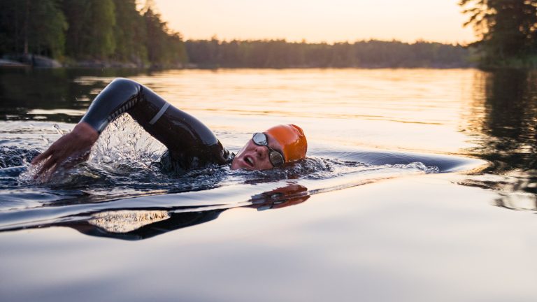 Eine Person in einem Neoprenanzug schwimmt in einem großen See. Eine Person in einem Neoprenanzug schwimmt in einem großen See.