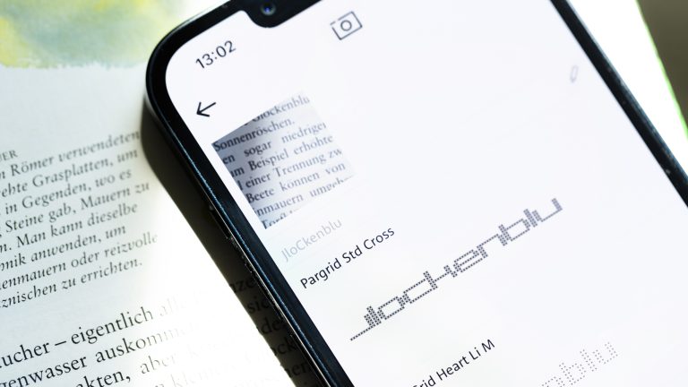 Ein iPhone mit der geöffneten WhatTheFont-App liegt auf einer Buchseite.
