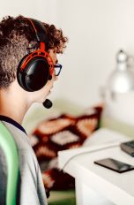 Eine Person in einem Gaming-Stuhl sitzt mit Headset auf dem Kopf vor einem Rechner.
