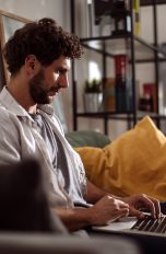 Eine Person sitzt mit einem MacBook auf dem Sofa.