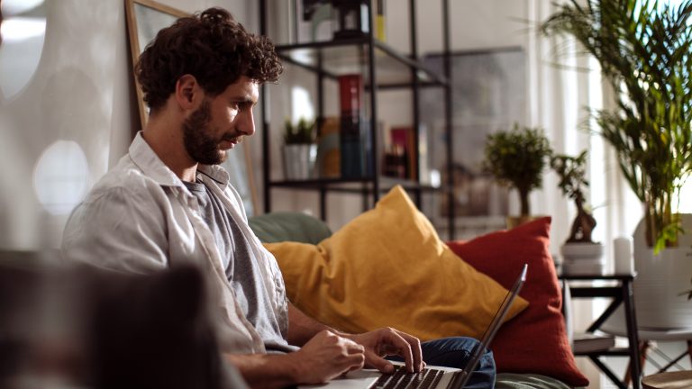 Eine Person sitzt mit einem MacBook auf dem Sofa.
