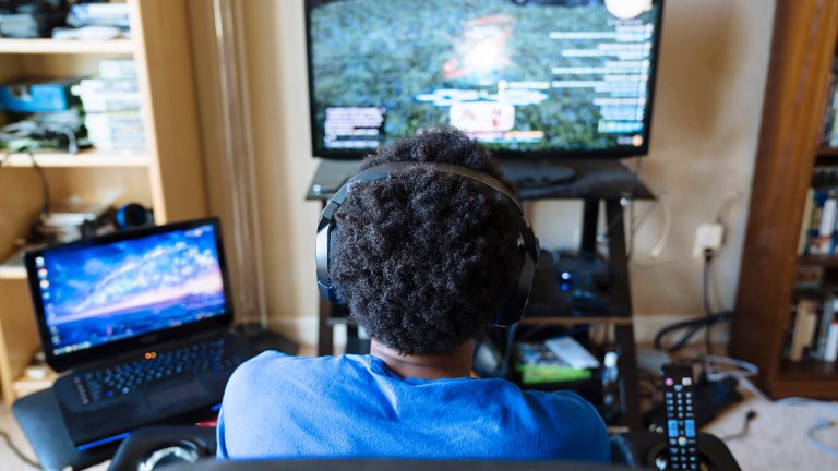 Eine Person sitzt vor einem Fernseher und spielt Final Fantasy XIV auf einem angeschlossenen PC.