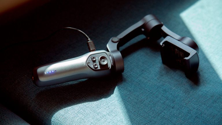 Ein Gimbal liegt auf einem Sofa und wird über eine USB-Kabel aufgeladen.