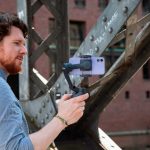 Eine Person hält einen Gimbal in der Hand, in den ein iPhone 12 eingesetzt ist.