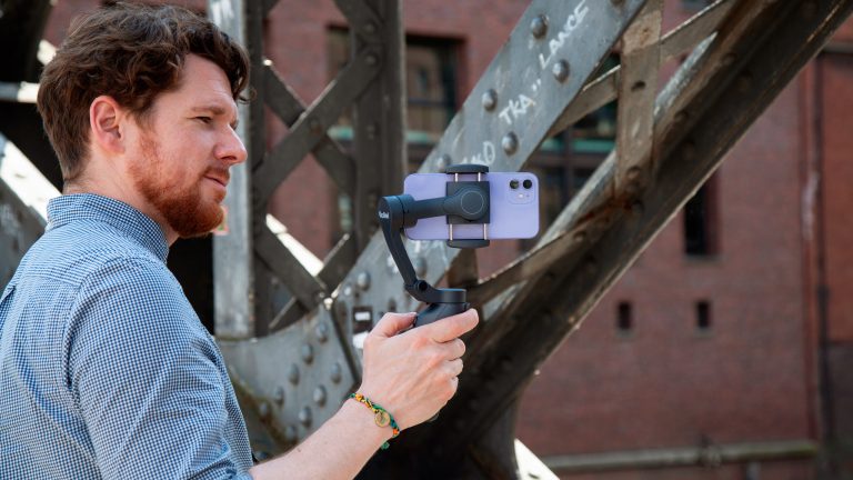 Eine Person hält einen Gimbal in der Hand, in den ein iPhone 12 eingesetzt ist.
