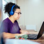 Eine Person mit Kopfhörern sitzt vor einem Laptop.