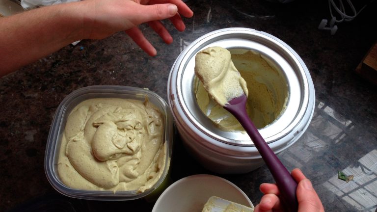 Eine Person entnimmt einem Behälter Eis und schöpft es in eine verschließbare Plastikschale. 
