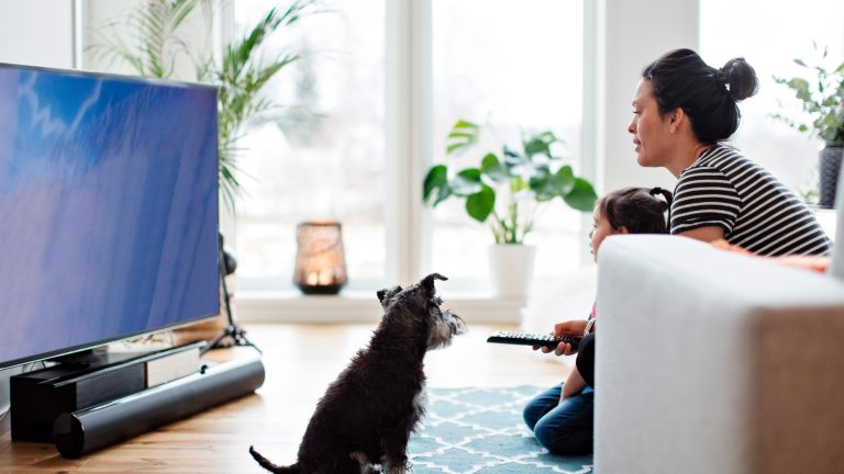 Fernseher-Größe, So findest du die ideale heraus Eine Person sitzt mit einem Kind vor einem Fernseher, der auf dem Boden steht.