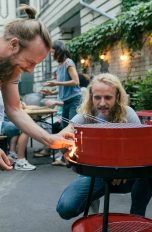 Zwei Personen stehen um einen Grill und entzünden diesen.