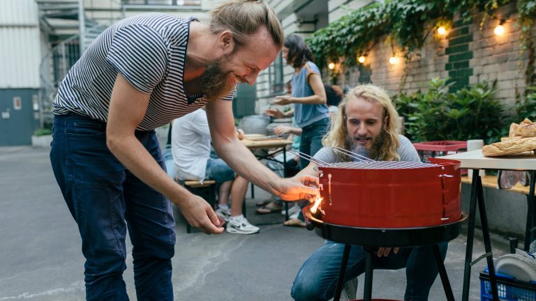 Zwei Personen stehen um einen Grill und entzünden diesen.