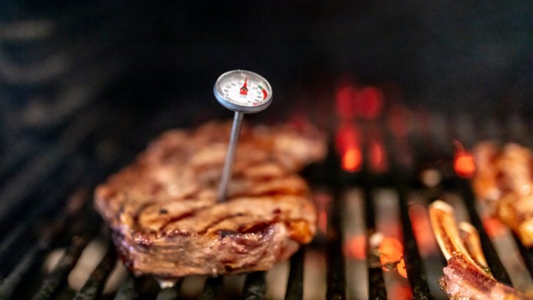 In einem Stück Fleisch, das auf einem Grill liegt, steckt ein Fleischthermometer.