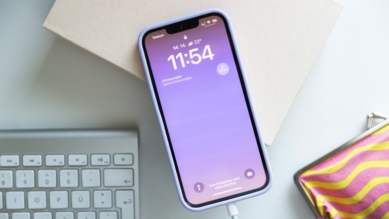 Ein iPhone 13 liegt zwischen mehreren Deko-Elementen und wird über ein Lightning-Kabel aufgeladen.