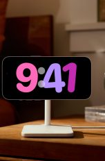 Ein iPhone 14 Pro hängt im Querformat auf einer Ladestation auf einem Nachttisch und zeigt die Uhrzeit an.