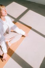 Eine Person sitzt vor einem Fenster im Licht am Boden und meditiert.