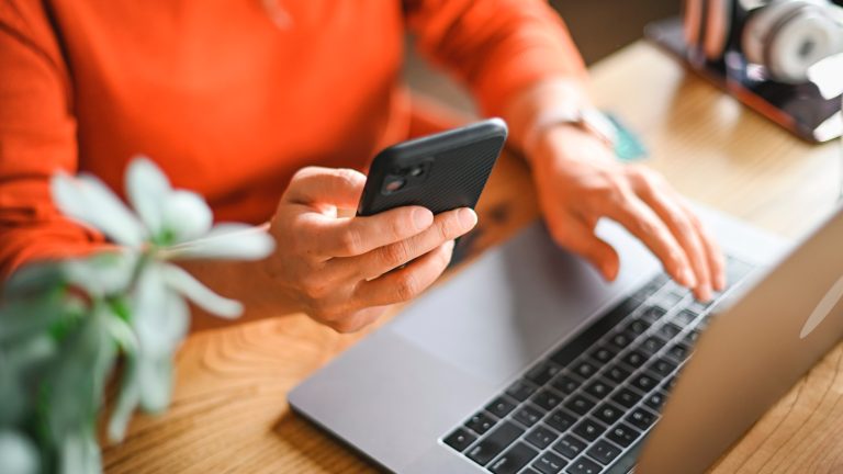 Fotos von iPhone auf PC und Mac übertragen: So klappt es Eine Person hält ein iPhone in der Hand und bedient mit der anderen ein MacBook Pro.