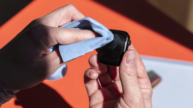 Eine Person reinigt mit einem Mikrofasertuch das Display der Apple Watch.