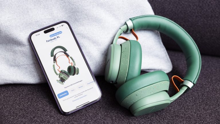Fairbuds XL in Grün liegen neben einem iPhone, auf dem die Explosionsansicht in der App zu sehen ist.