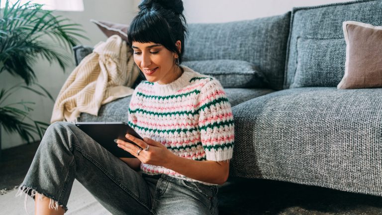 Eine Person sitzt vor einem Sofa auf dem Boden und schaut auf ein Tablet.