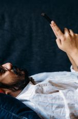 Eine Person liegt auf einem Sofa und schaut auf das Smartphone in ihren Händen.