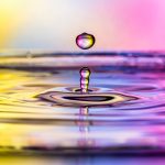 Nahaufnahme eines Wassertropfens, der von einer mit Wasser bedeckten Oberfläche nach oben prallt.