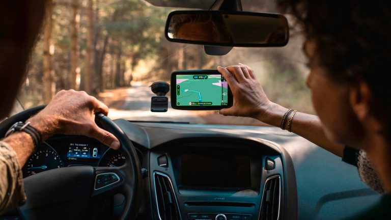 Zwei Personen sitzen in einem Auto. Eine davon hängt ein Navigationssystem in seine Scheibenhalterung.