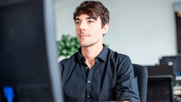 Eine Person im blauen Hemd sitzt vor einem PC.