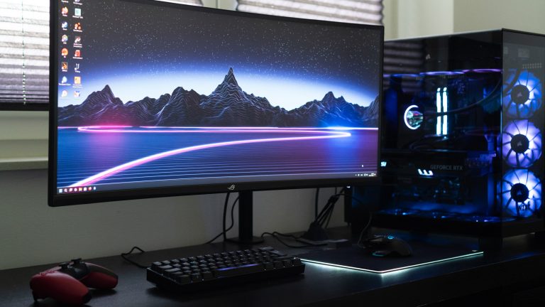 Auf einem Ultrawide-Monitor ist ein Windows-10-Desktop zu sehen. Neben dem Monitor steht ein Gaming-PC mit beleuchteten Lüftern. Auf einem Ultrawide-Monitor ist ein Windows-10-Desktop zu sehen. Neben dem Monitor steht ein Gaming-PC mit beleuchteten Lüftern.