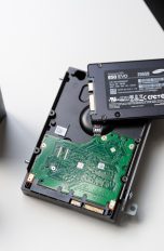 Eine klassische HDD-Festplatte liegt auf einem Tisch. Auf der HDD liegt eine deutlich kleinere SSD-Festplatte.