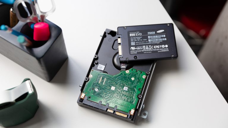 Eine klassische HDD-Festplatte liegt auf einem Tisch. Auf der HDD liegt eine deutlich kleinere SSD-Festplatte.