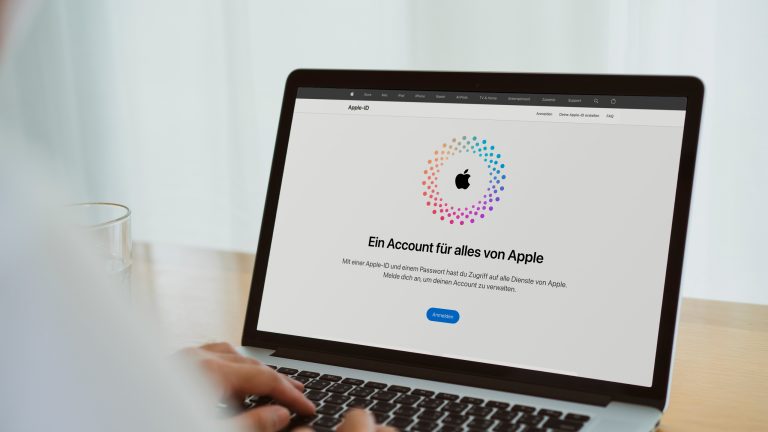 Eine Person sitzt vor einem MacBook. Auf dem Bildschirm ist die Anmeldeseite zur Apple-ID zu sehen.