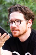 Eine Person hält ein Smartphone vor ihr Gesicht und nimmt eine Sprachnachricht auf.