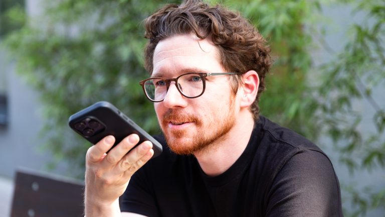 Eine Person hält ein Smartphone vor ihr Gesicht und nimmt eine Sprachnachricht auf.