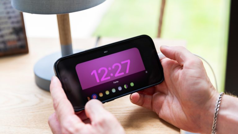 Eine Person hält ein iPhone 14 Pro in den Händen, auf dem gerade die Bearbeitungsoptionen des Standby-Modus zu sehen sind.