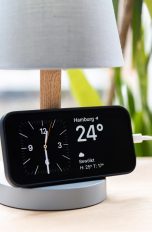 Ein iPhone 14 Pro lehnt an einer Tischlampe und zeigt den neuen Standby-Modus.