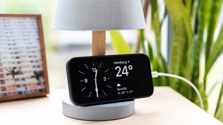 Ein iPhone 14 Pro lehnt an einer Tischlampe und zeigt den neuen Standby-Modus.