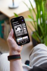 Eine Person hält ein iPhone in der Hand, auf dem die Musik-App im Dunkelmodus angezeigt wird.