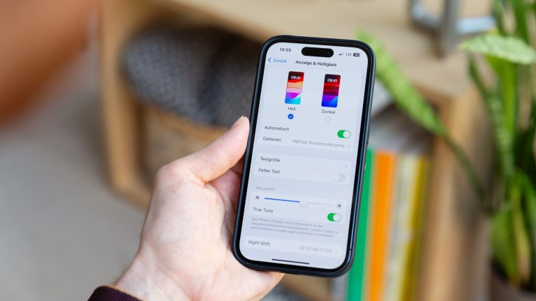 Eine Person hält ein iPhone in der Hand, auf dem die Einstellungen für den Dunkelmodus geöffnet sind.
