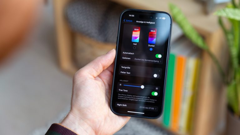 Eine Person hält ein iPhone in der Hand, auf dem die Einstellungen für den Dunkelmodus geöffnet sind.