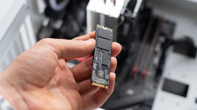 Eine Person hält eine M.2-SSD über einen geöffneten Desktop-PC.
