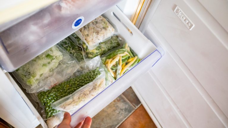 Young Man Opening Freezer With Frozen Vegetables Inside Eine Person zieht ein Fach in einem Gefrierschrank heraus.